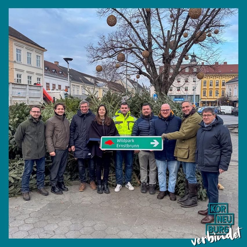 Gruppe von Menschen vor einem Straßenschild mit Richtung Ernstbrunn und einem Weihnachtsbaum im Hintergrund.