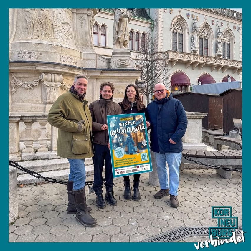 Vier Personen stehen vor einem historischen Gebäude. Sie lächeln und halten ein Plakat mit den Worten Winter Wonderland in der Hand.