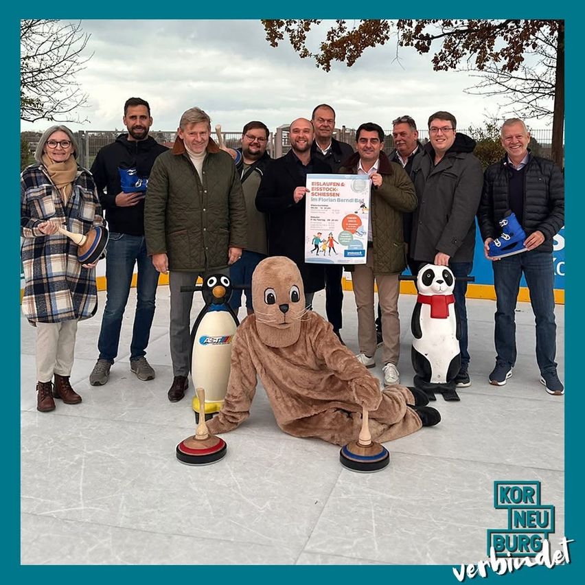 Eine Gruppe von Menschen, die auf einer Eisbahn steht und mit einer Maskottchen für ein Foto posiert, hält ein Plakat mit Text und einer Pinguin-Skulptur.