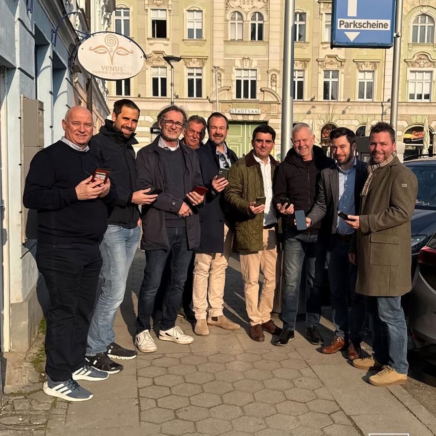 A group of men are standing outside, holding awards. They are smiling and posing for a photo in front of a building.