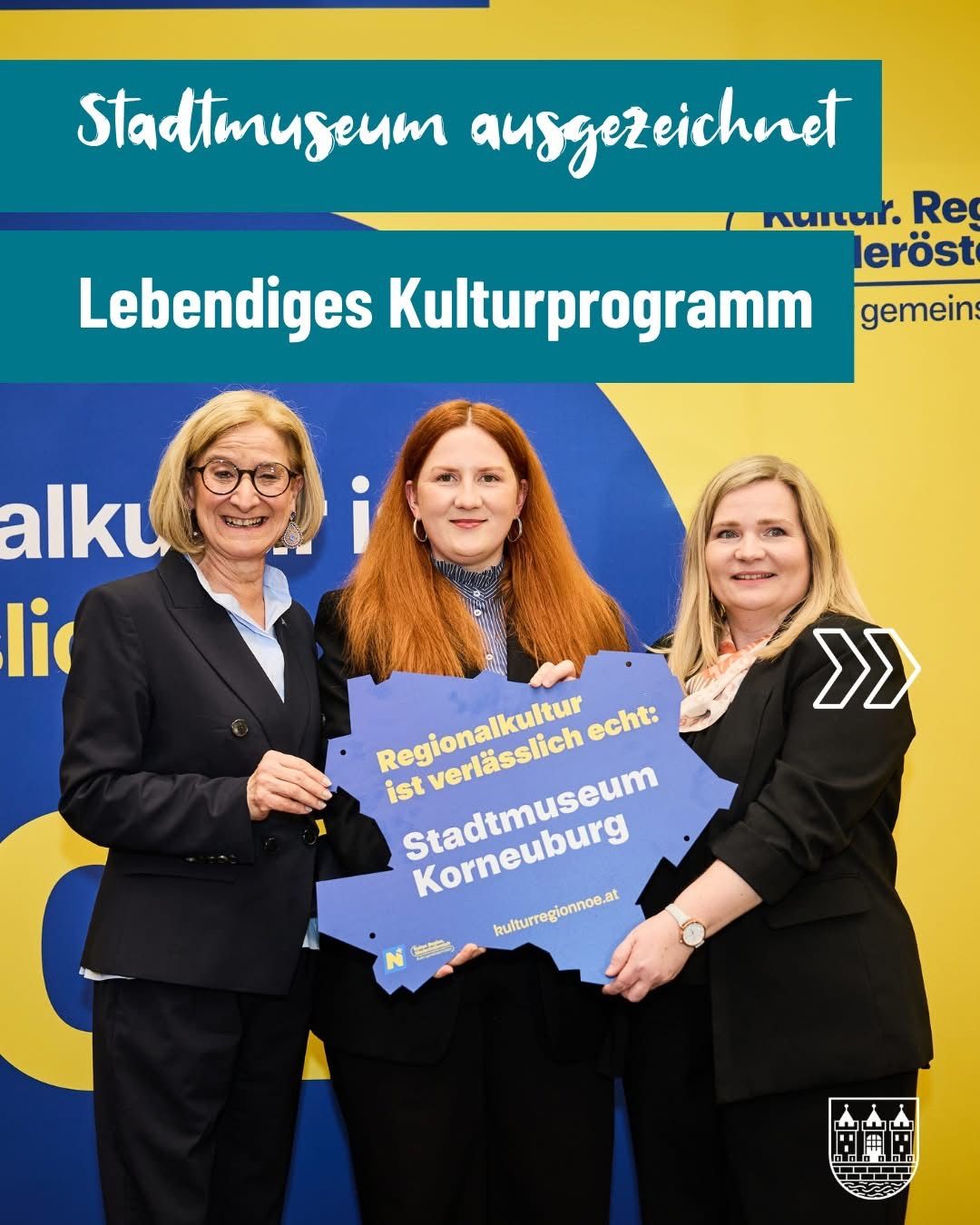Three women stand smiling in front of a blue sign reading 'Regionalkultur echt: Stadtmuseum Krems'. They are at an event with a yellow and blue backdrop and text that reads 'Lebendiges Kulturprogramm'.