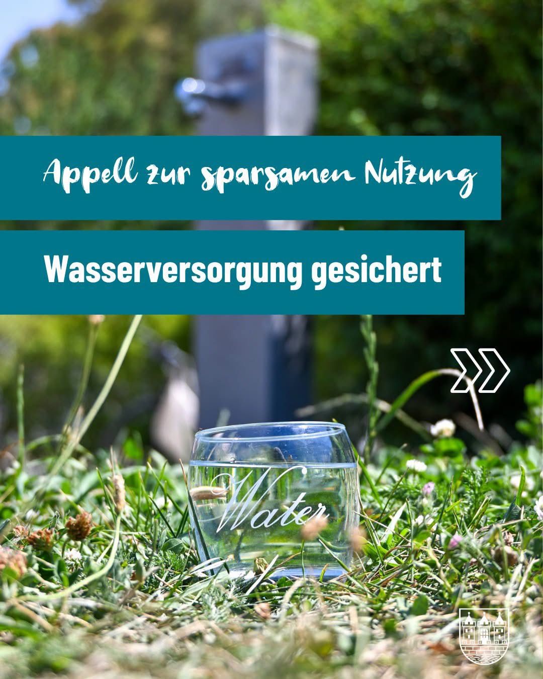 Ein Glas Wasser auf einem Grasfeld mit einem blauen Banner darüber, das 'Appell zur sparsamen Nutzung' und 'Wasserversorgung gesichert' steht. Das Wort 'Wasser' ist in das Glas geätzt.