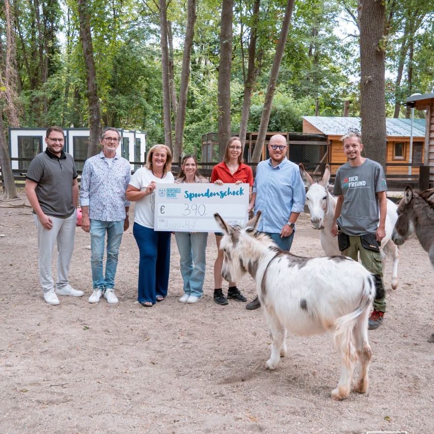 Eine Gruppe von Menschen, die einen großen Scheck halten und mit Eseln in einem Zoo posieren.