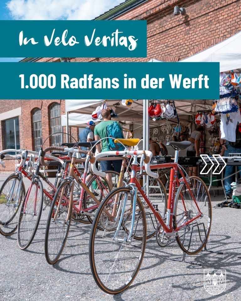 Fahrräder in einer Reihe unter einem Zelt mit dem Schild '1.000 Radfans in der Wert'. Menschen im Hintergrund, einige tragen Mützen und haben Taschen.