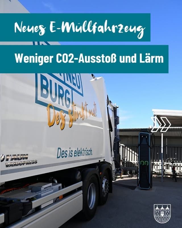 Ein elektrischer Müllwagen mit Burg-Logo steht neben einer Ladestation unter blauem Himmel.
