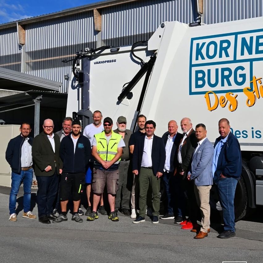 Eine Gruppe von Männern steht vor einem weißen Müllwagen mit dem Text 'Kornburg Des'. Sie sind in verschiedenen Outfits gekleidet.