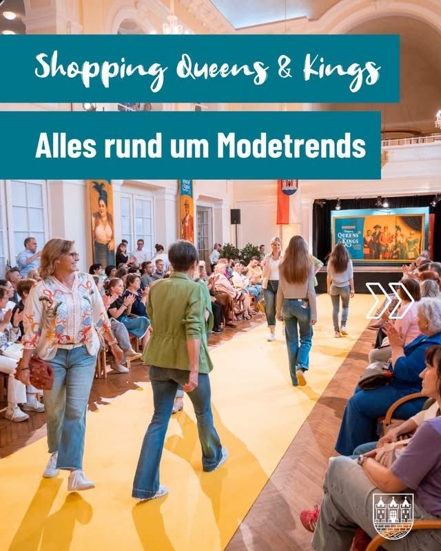 Ein Modeevent mit Frauen, die auf einem gelben Teppich laufen. Zuschauer sitzen in Reihen und beobachten die Veranstaltung. Im Hintergrund befindet sich eine Bühne mit einer großen Leinwand.