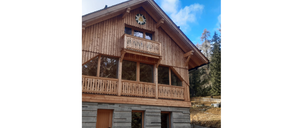 Ein Holzchalet mit einem dreieckigen Dach und einem Balkon, der mit einem Blumendesign über dem Eingang verziert ist.