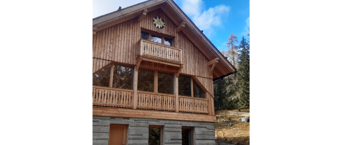 Ein Holzchalet mit einem dreieckigen Dach und einem Balkon, der mit einem Blumendesign über dem Eingang verziert ist.