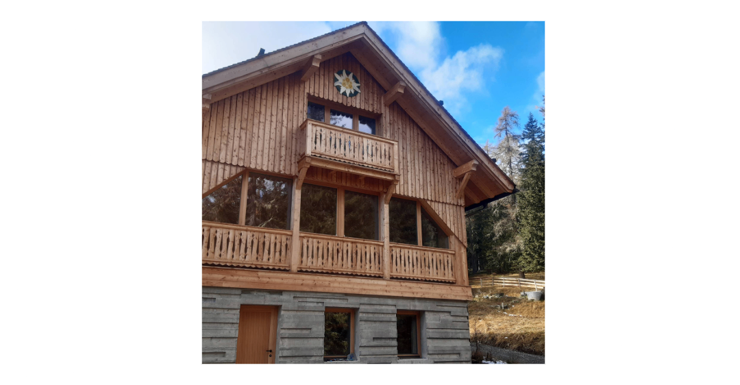 Ein Holzchalet mit einem dreieckigen Dach und einem Balkon, der mit einem Blumendesign über dem Eingang verziert ist.
