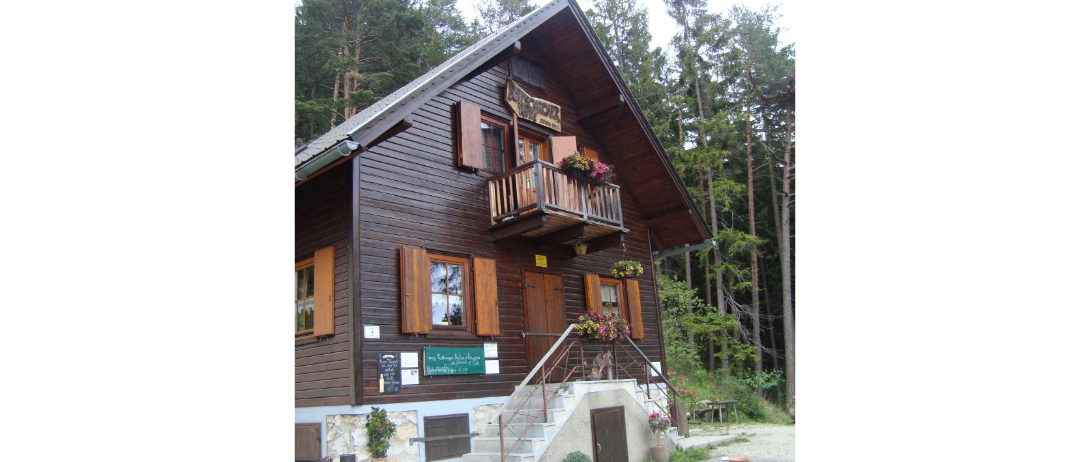 Ein Holzhaus mit mehreren Fenstern und einem Balkon, geschmückt mit Blumen, in einem Waldgebiet gelegen.