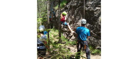 Mehrere Personen sind beim Klettern. Eine Frau steigt mit einem Seil ab, während ein Mann das Seil hält. Ein anderer Kletterer ist oben.