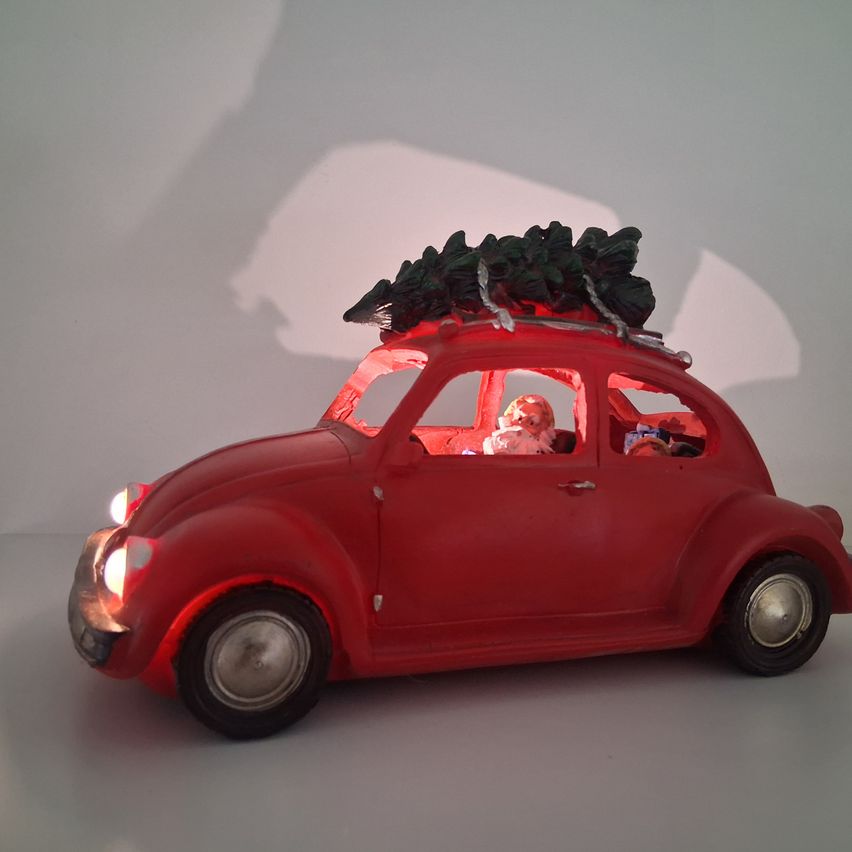 Ein rotes Spielzeugauto mit einem Weihnachtsbaum auf dem Dach, beleuchtet von roten Lichtern. Es hat eine Figur darin, möglicherweise der Weihnachtsmann.