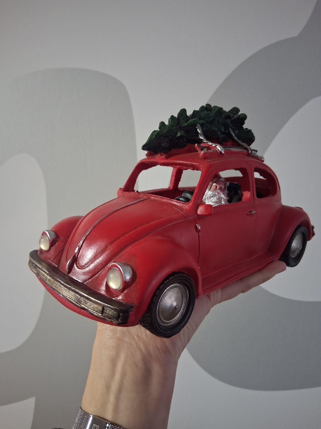 Ein rotes Spielzeugauto mit einem Weihnachtsbaum auf dem Dach wird von einer Hand gehalten. Das Auto ist mit einer Santa-Claus-Figur auf dem Fahrersitz dekoriert.