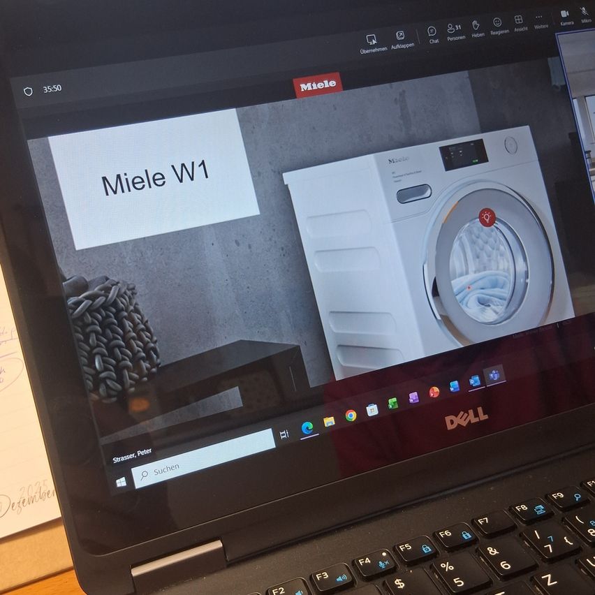 Ein Laptop-Bildschirm zeigt eine Miele W1 Waschmaschine. Der Laptop ist offen und zeigt eine Suchleiste mit 'Straße, Peter' eingegeben. Der Bildschirm hat verschiedene Symbole und eine Zeitangabe von 35:50.