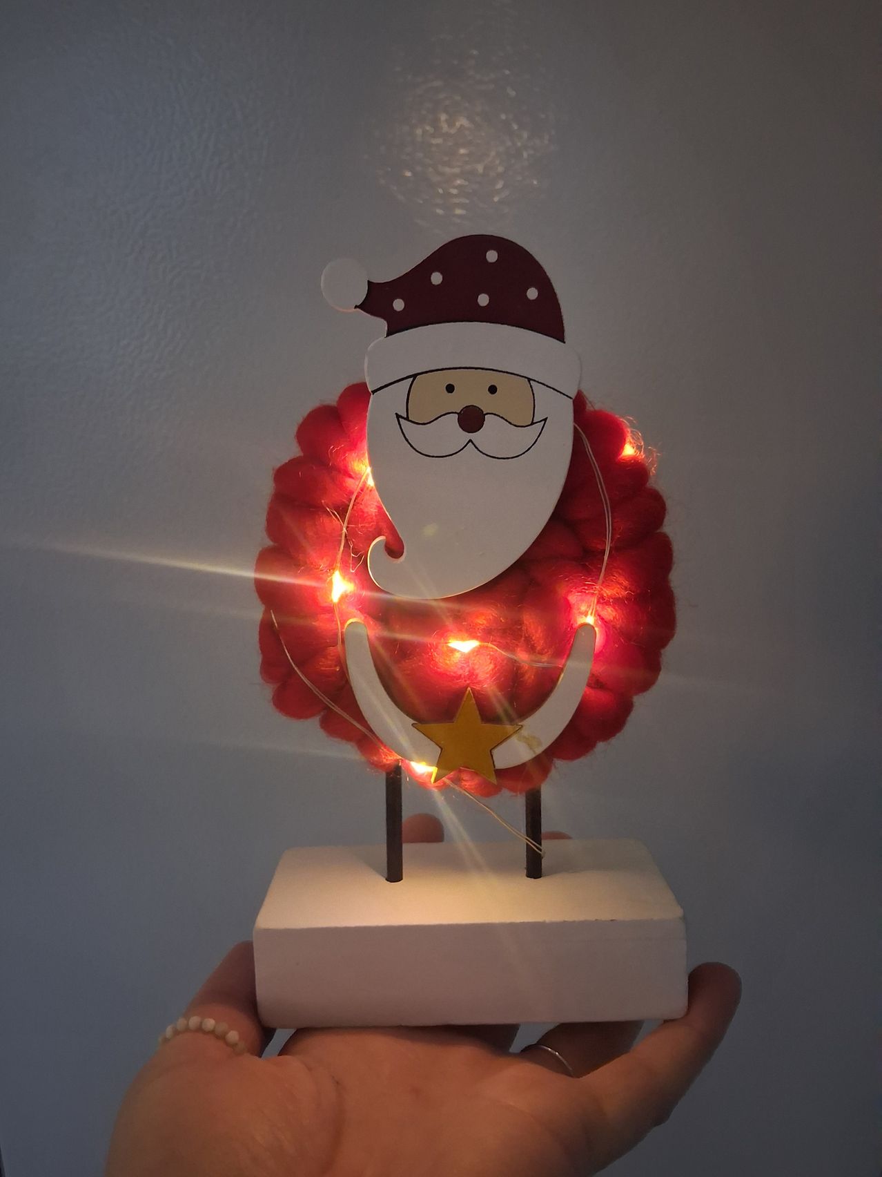 Ein kleines dekoratives Item von Santa Claus in Form einer Krone mit rotem Hintergrund und leuchtenden Lichtern wird in der Hand gehalten.