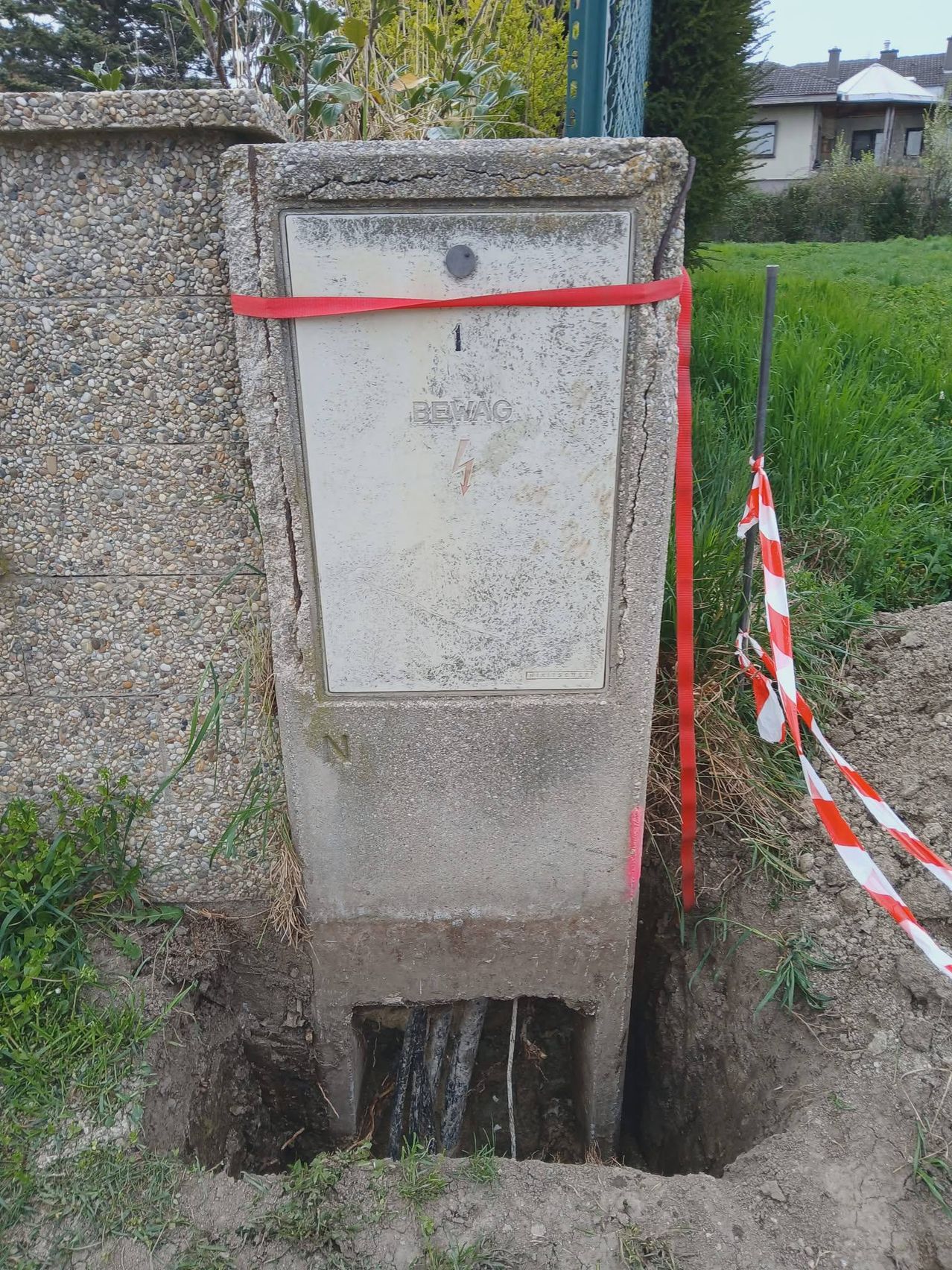A concrete box with the number 1 is secured with a red ribbon, partially buried in the ground.