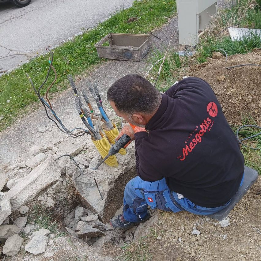 A man works on an underground utility project. He's drilling into the ground, surrounded by tools and wires.