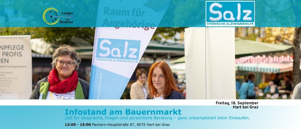 Zwei Frauen stehen vor einem Banner der Steirischen Alzheimerhilfe, mit einem Markt im Hintergrund. Das Banner trägt die Aufschrift 'Raum für Angehörige' und 'Salz'. Die Frauen lächeln und scheinen in ein Gespräch vertieft zu sein.