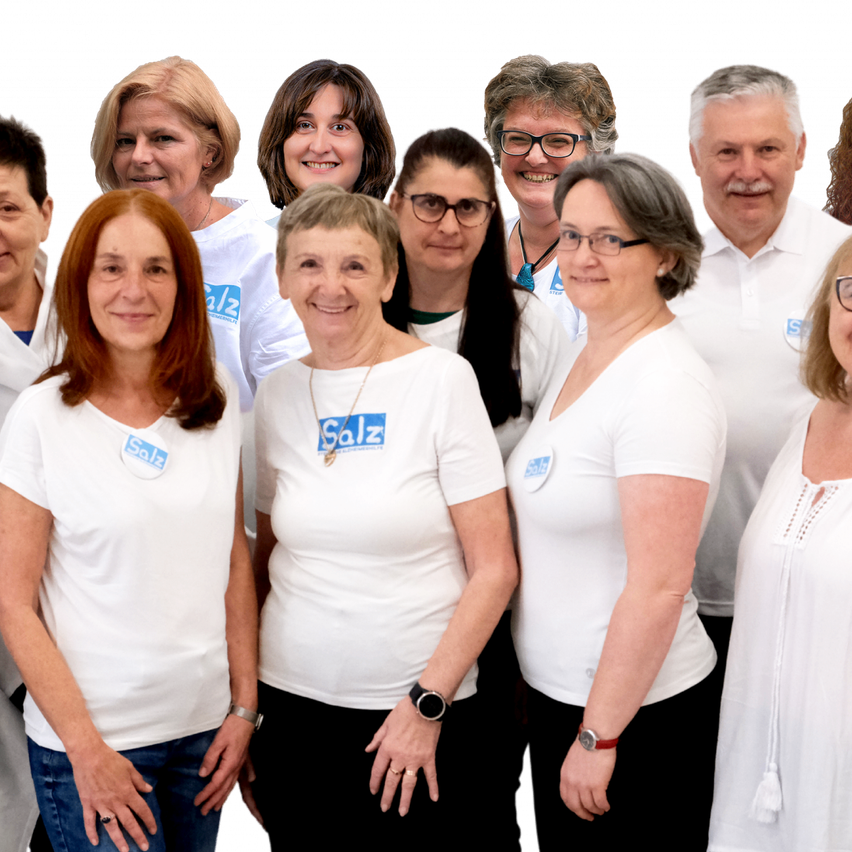 Eine Gruppe von Personen in weißen T-Shirts mit blauen Logos steht zusammen, lächelt und posiert für ein Foto. Sie tragen alle Brillen und Uhren.