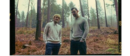 Ein Plakat mit einem Foto von zwei Männern im Wald. Der Titel lautet 'KONZERT'. Unten steht Datum, Uhrzeit und Veranstaltungsort. Der Eintritt kostet EUR 15.