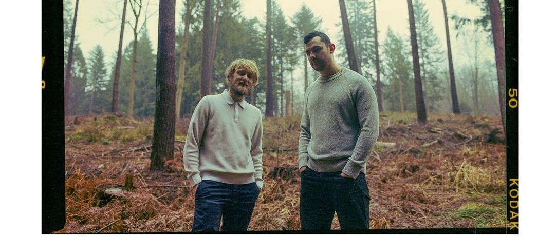 Ein Plakat mit einem Foto von zwei Männern im Wald. Der Titel lautet 'KONZERT'. Unten steht Datum, Uhrzeit und Veranstaltungsort. Der Eintritt kostet EUR 15.