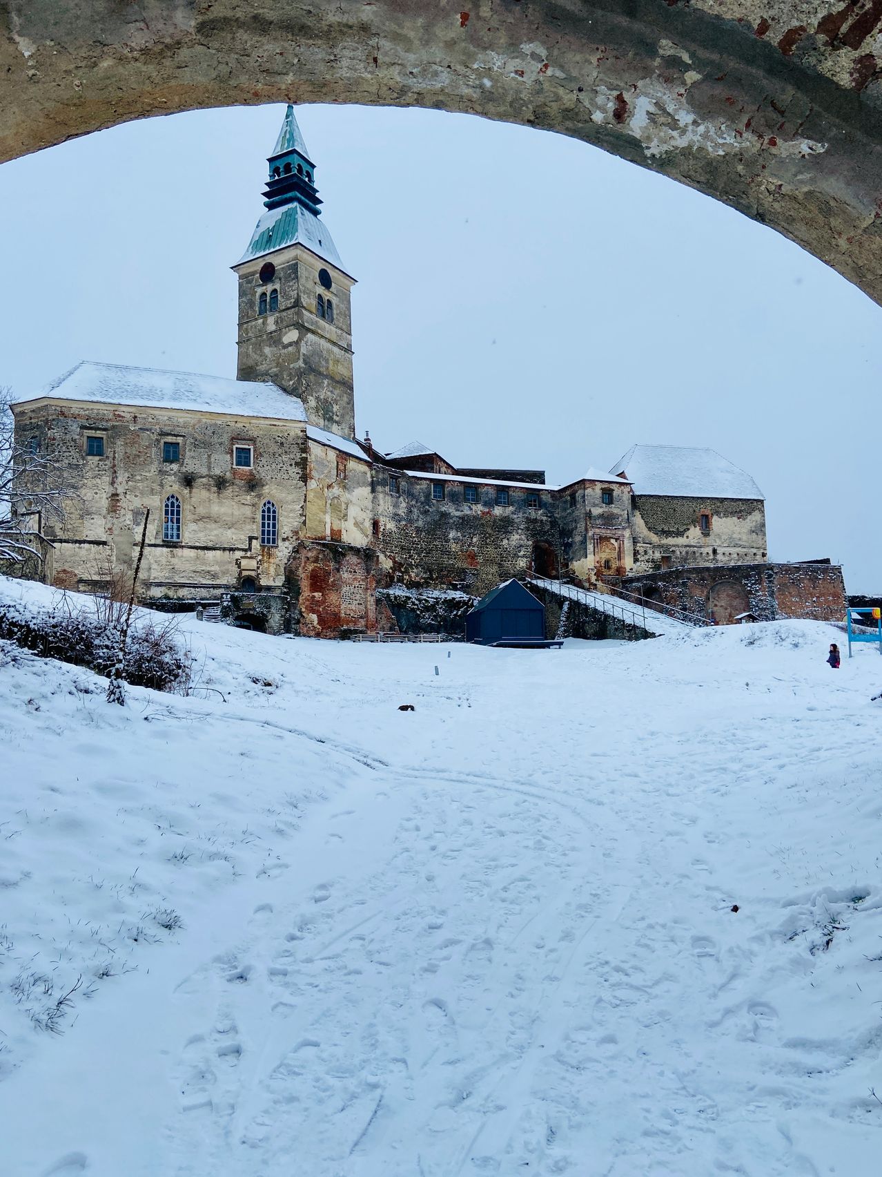 Eine schneebedeckte Burg mit einem hohen Turm steht auf einem Hügel. Ein kleines blaues Zelt ist in der Nähe. Der Boden ist mit Schnee bedeckt.
