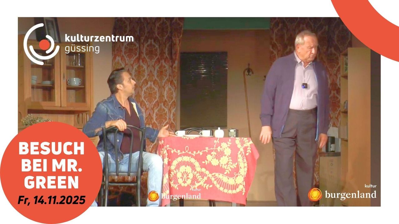 Two men in a dining room with a table covered in a red tablecloth. One man looks at another. Text reads 'urzentrum'.