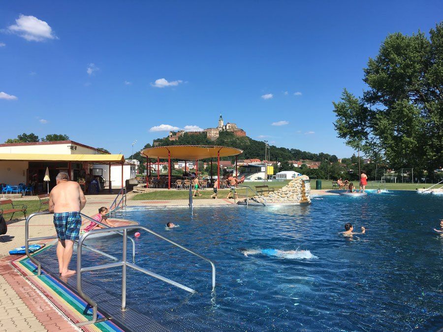 Outdoor swimming pool with people swimming and a castle in the background under a clear sky.