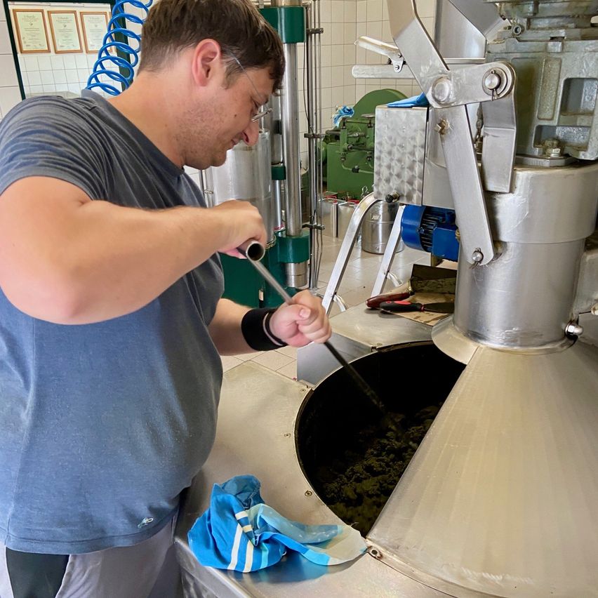 A man is cleaning a large metal machine with a tool in what appears to be a factory.