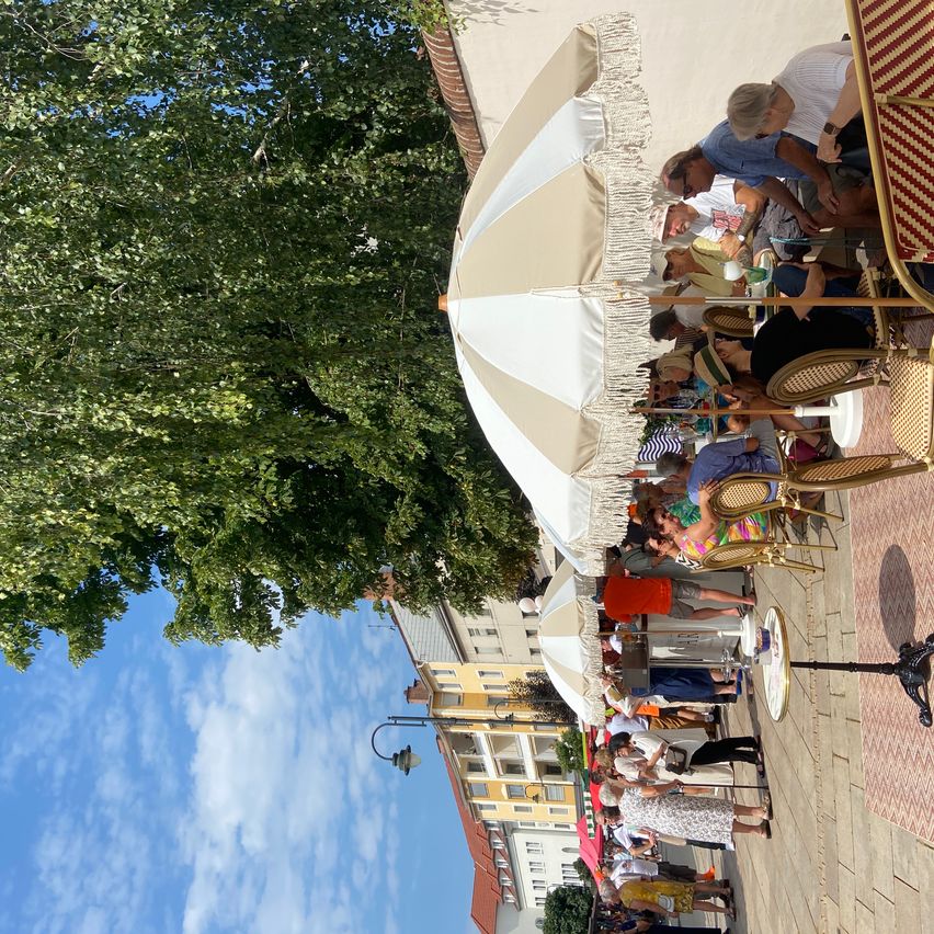 Eine Gruppe von Menschen versammelt sich unter Sonnenschirmen in einem Café im Freien und genießt den sonnigen Tag.