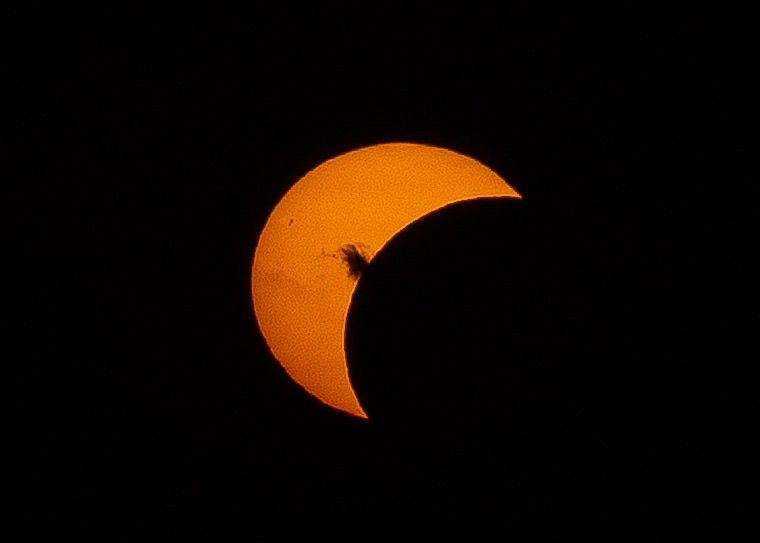 A partial solar eclipse with a bright orange sun partially covered by the moon.
