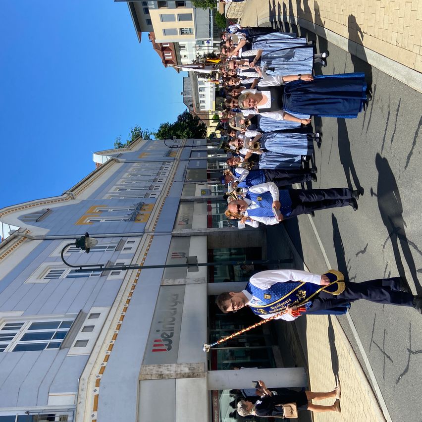 A marching band practices in a city. The building in the background has a sign reading 'Städtisches Theater'.