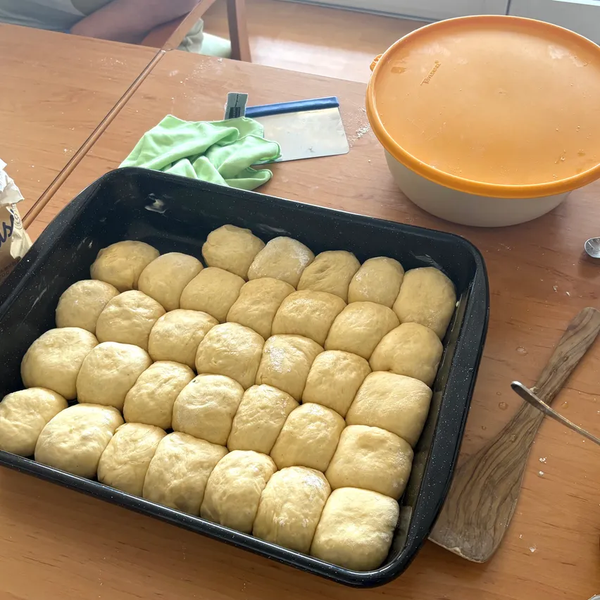 Ein Tablett mit runden Teigbällen, bereit zum Backen, steht auf einem Holztisch mit einem Schüssel und einem Spatel in der Nähe.