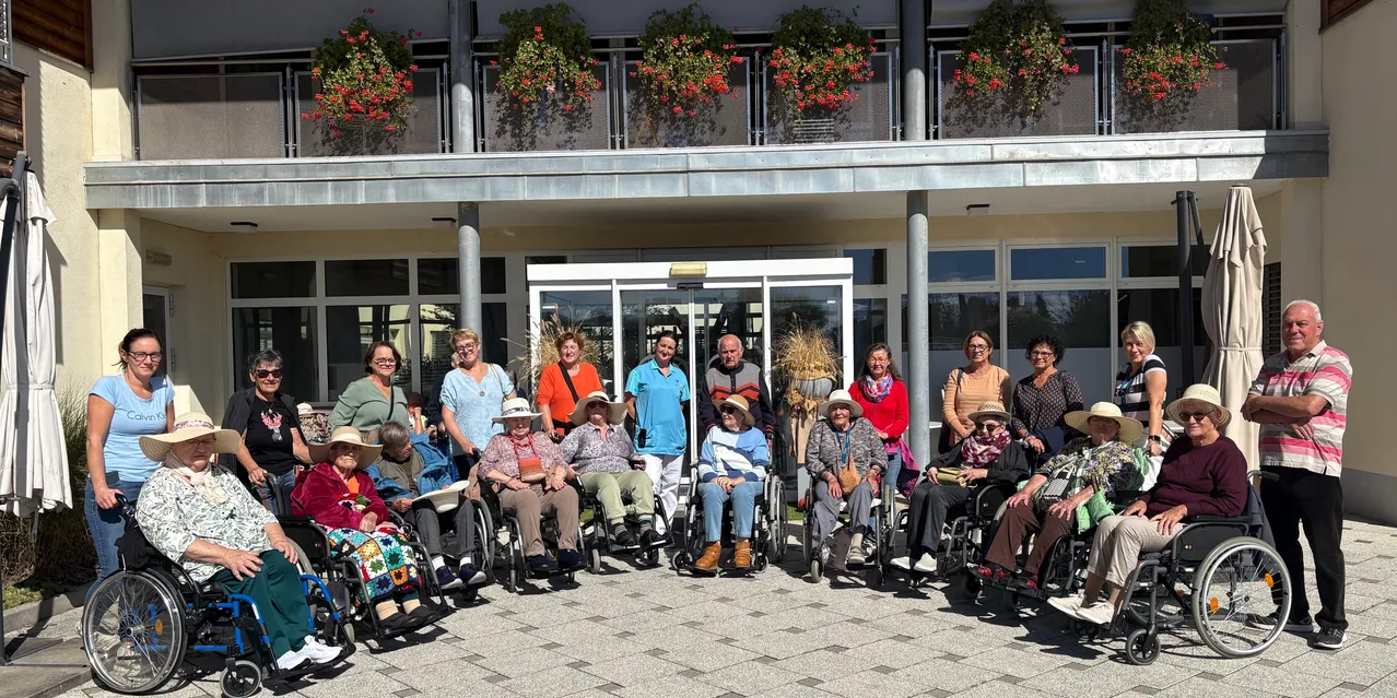 Eine Gruppe älterer Menschen in Rollstühlen posiert für ein Foto vor einem Gebäude mit roten Blumen.