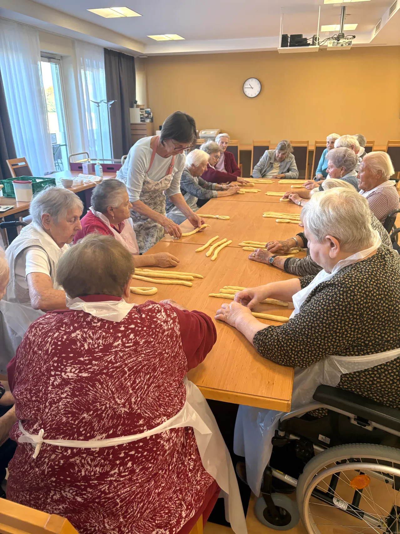 Eine Gruppe älterer Frauen sitzt um einen Tisch herum und ist mit einer Pasta-Herstellungsaktivität beschäftigt.