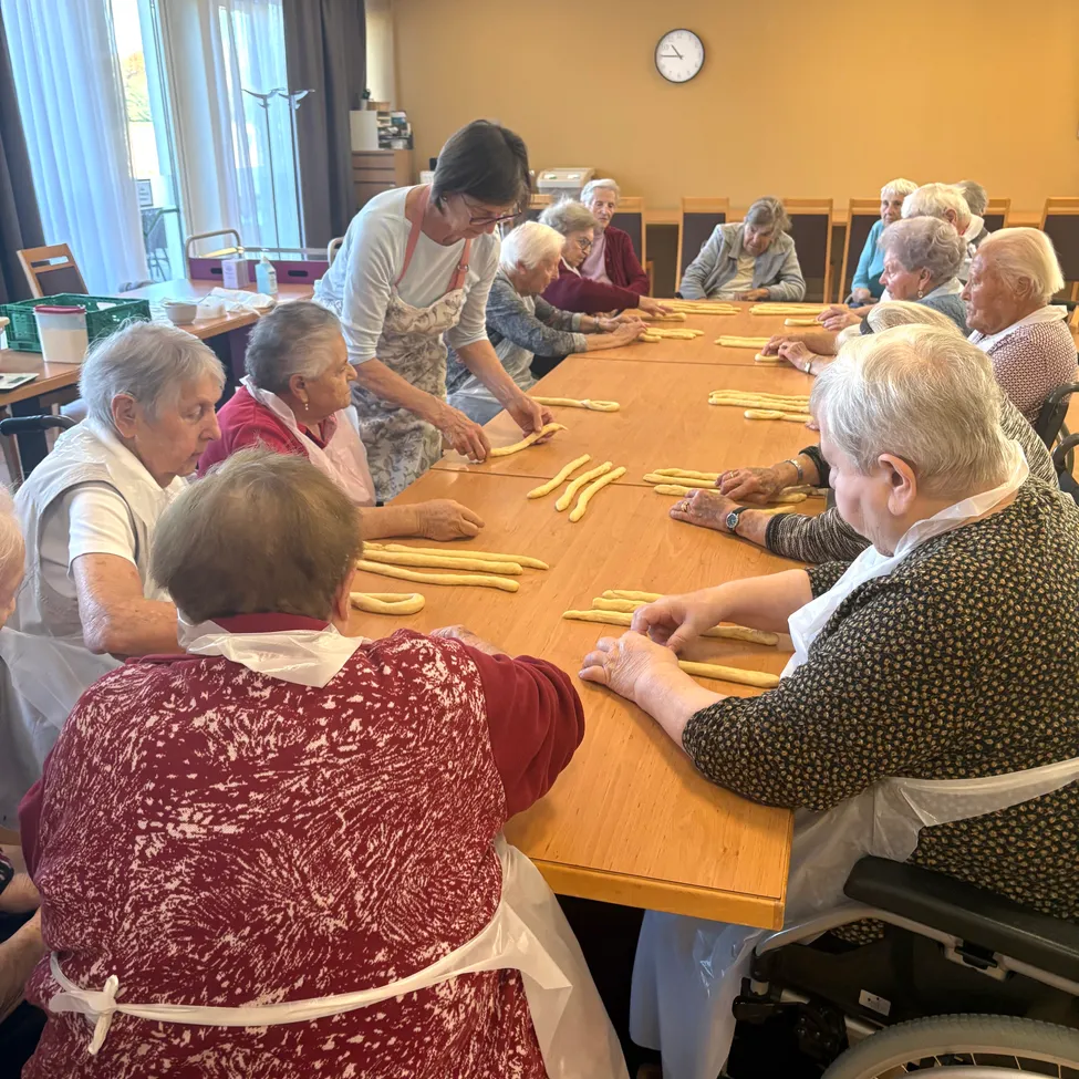 Eine Gruppe älterer Frauen sitzt um einen Tisch herum und ist mit einer Pasta-Herstellungsaktivität beschäftigt.