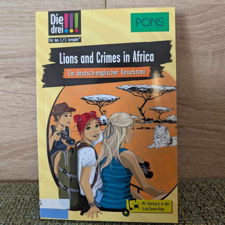 Buchcover mit dem Titel 'Lions and Crimes in Africa'. Es zeigt drei Frauen, eine mit Rucksack und Fernglas, eine andere mit Fernglas und einen Löwen im Hintergrund. Das Buch ist für das Alter von 2/3 Jahren und enthält Audio.