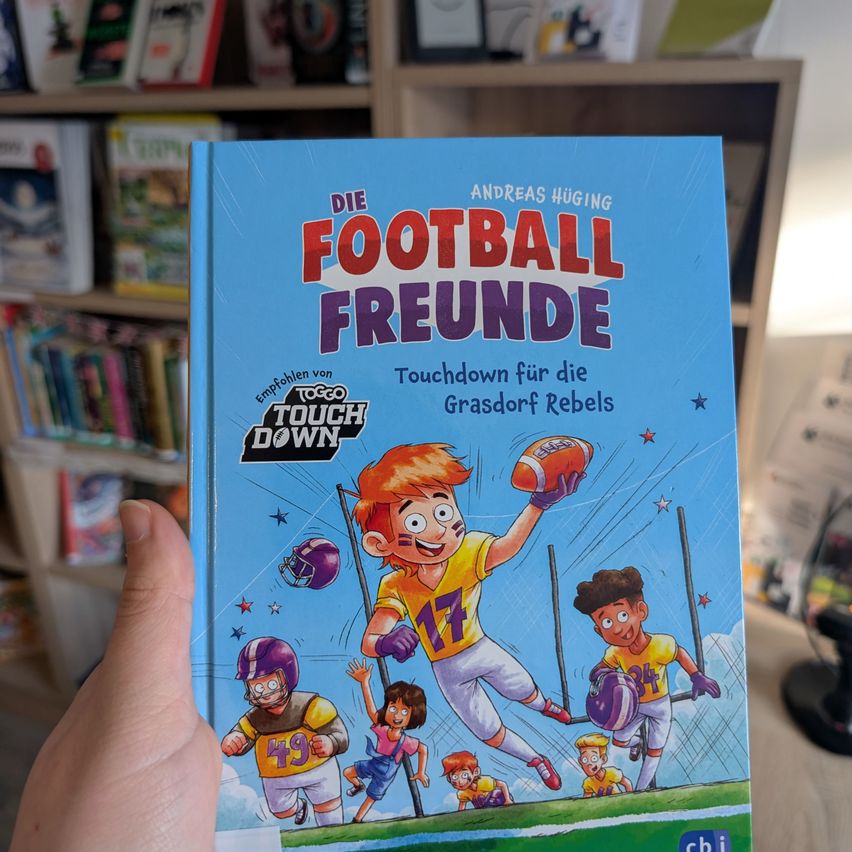 Ein Buchcover zeigt einen Jungen in einem Football-Trikot, der einen Ball fängt. Es steht 'Die Football Freunde Touchdown für die Grasdorf Rebels'.
