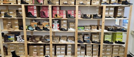 Ein Schuhgeschäft mit Regalen voller Stiefel, Sneaker und verschiedener anderer Schuhtypen in verschiedenen Farben und Größen. Hinter den Regalen sind Schuhkartons gestapelt.