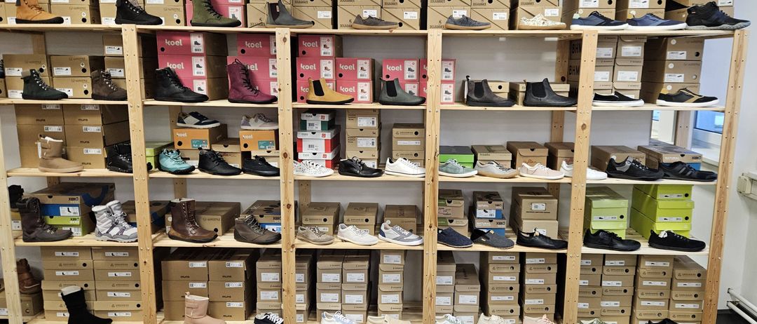 Ein Schuhgeschäft mit Regalen voller Stiefel, Sneaker und verschiedener anderer Schuhtypen in verschiedenen Farben und Größen. Hinter den Regalen sind Schuhkartons gestapelt.