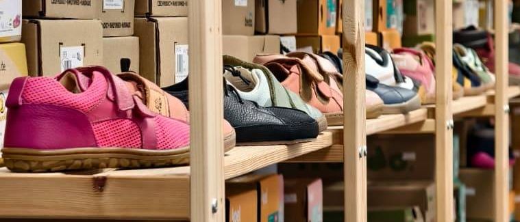 Reihen von Holzregalen gefüllt mit bunten Kinderschuhen, einige in ihren Kartons, andere getragen und ausgestellt. Die Regale sind mit verschiedenen Größen und Stilen bestückt und zeigen eine Reihe von Marken und Farben.