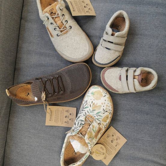 Fünf Paar Schuhe in verschiedenen Größen und Stilen sind auf einem grauen Stoff ausgelegt. Einige Schuhe haben Schnürsenkel, andere haben Klettverschlüsse. Alle Schuhe haben braune Sohlen und angebrachte Etiketten.