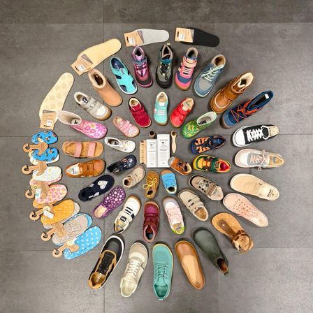 Ein Kreis verschiedener Kinderschuhe, auf einem gefliesten Boden angeordnet, einschließlich Turnschuhe, Sandalen und Stiefel, alle in verschiedenen Farben und Stilen.