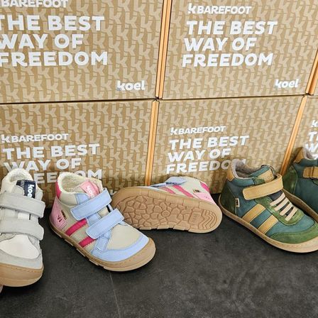 Drei Paar Kinderschuhe vor Schachteln mit der Aufschrift 'Der beste Weg der Freiheit' von Koel. Die Schuhe sind in verschiedenen Farben und Größen.