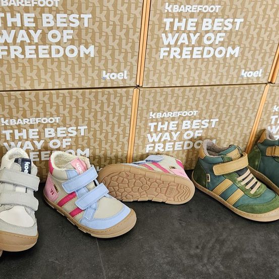 Drei Paar Kinderschuhe vor Schachteln mit der Aufschrift 'Der beste Weg der Freiheit' von Koel. Die Schuhe sind in verschiedenen Farben und Größen.