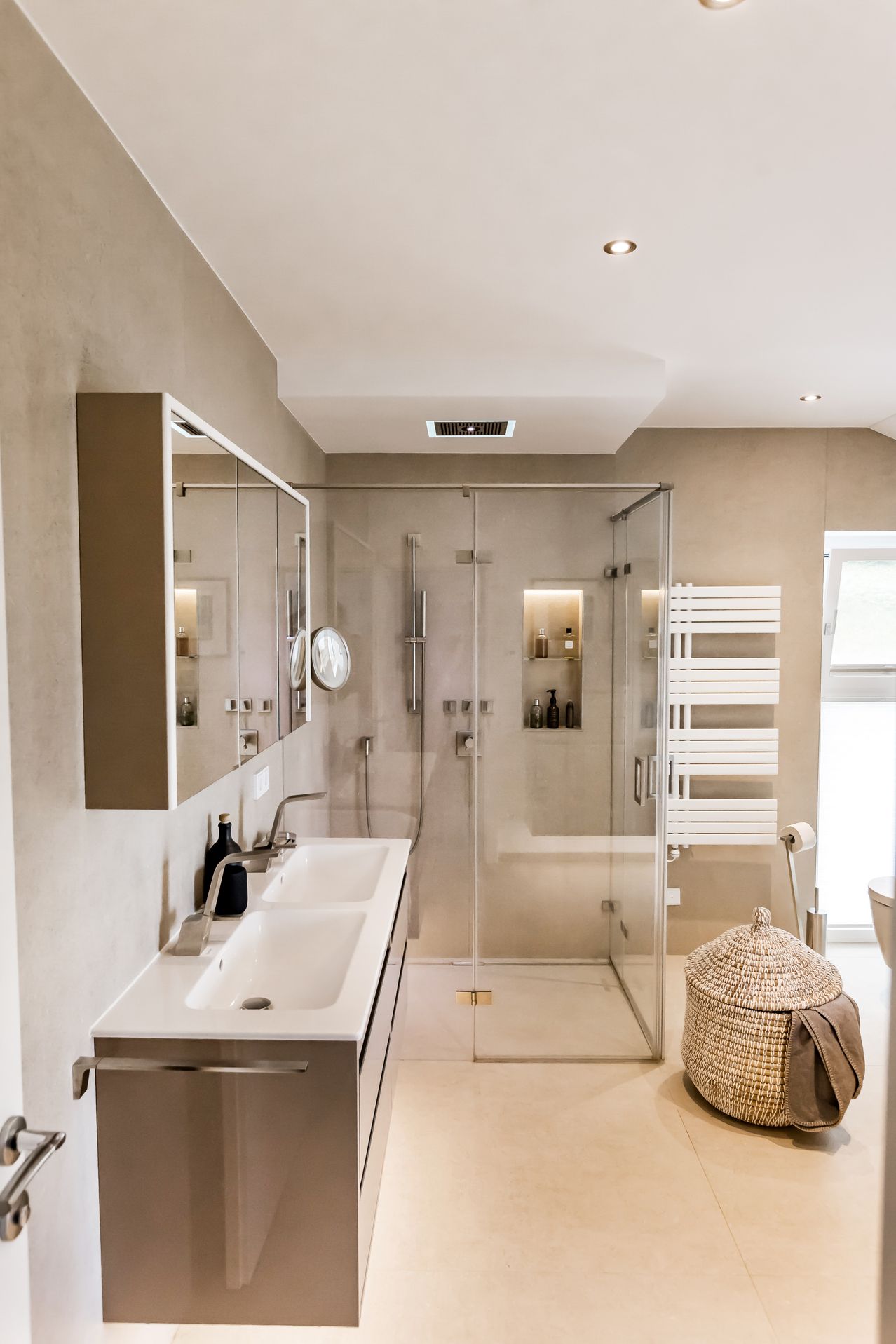 Ein Badezimmer mit einem weißen Waschbecken, einer Glasdusche und einem Handtuchhalter. Ein Spiegel und ein Schrank sind an der Wand montiert. Das Badezimmer hat ein modernes Design.
