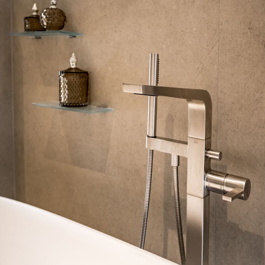 Ein modernes Badezimmer mit einer weißen Badewanne und einem Edelstahlhahn an der Wand. Zwei Glasregale mit dekorativen Gläsern sind an der Wand montiert.