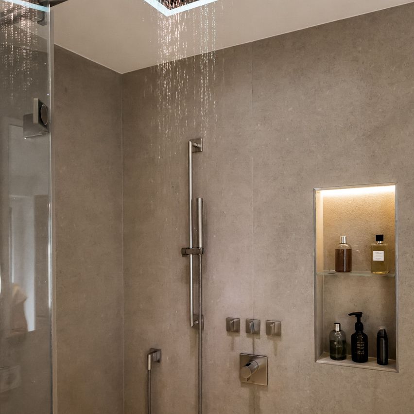 Moderner Duschbereich mit einem Regenduschkopf und eingebauten Nischen für Toilettenartikel. Die Dusche ist durch eine Glastür abgeschirmt.