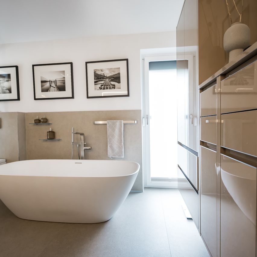 Ein modernes Badezimmer mit einer großen weißen Badewanne, einem weißen Handtuch an einem Handtuchhalter, drei gerahmten Bildern an der Wand und einer Tür, die in einen anderen Raum führt.